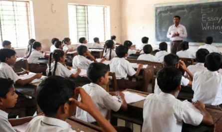 বিদ্যালয়ে শিক্ষার্থীরা খাতায় প্রবন্ধ লিখছে এবং শিক্ষক ব্ল্যাকবোর্ডে বিষয় বুঝিয়ে দিচ্ছেন